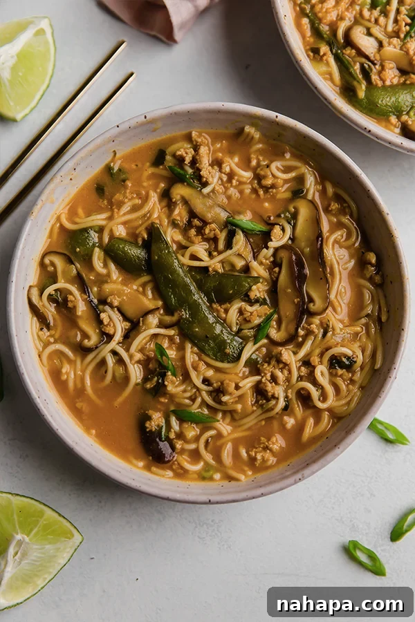 A close-up of a steaming bowl of creamy coconut curry ramen, garnished with fresh green onions and lime wedges, ready to be enjoyed.