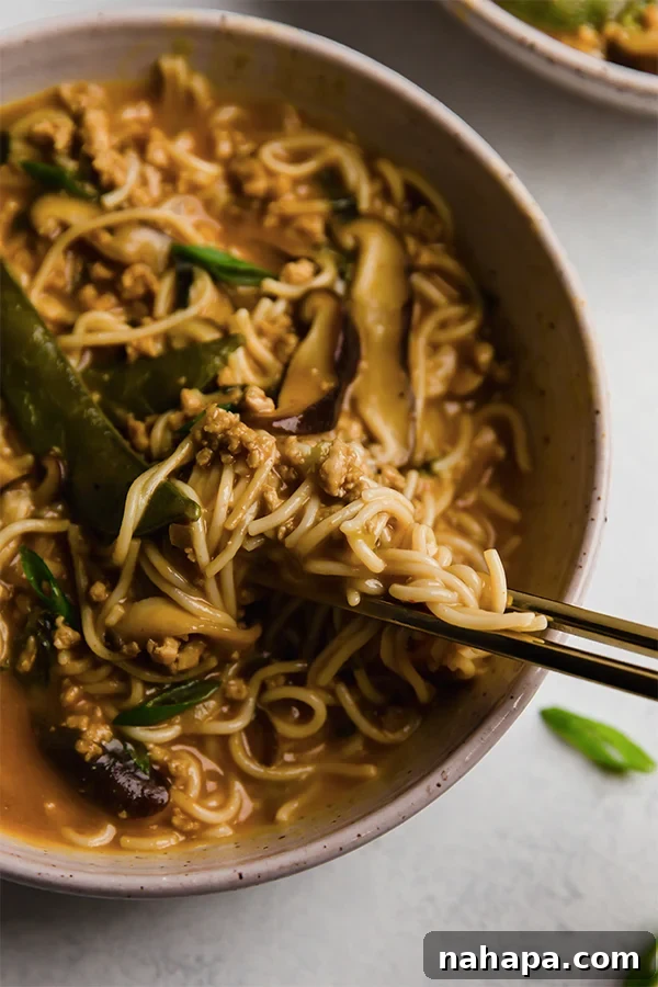 Chopsticks lifting a delicious bite of creamy coconut curry ramen, showing the noodles, pork, and vegetables.