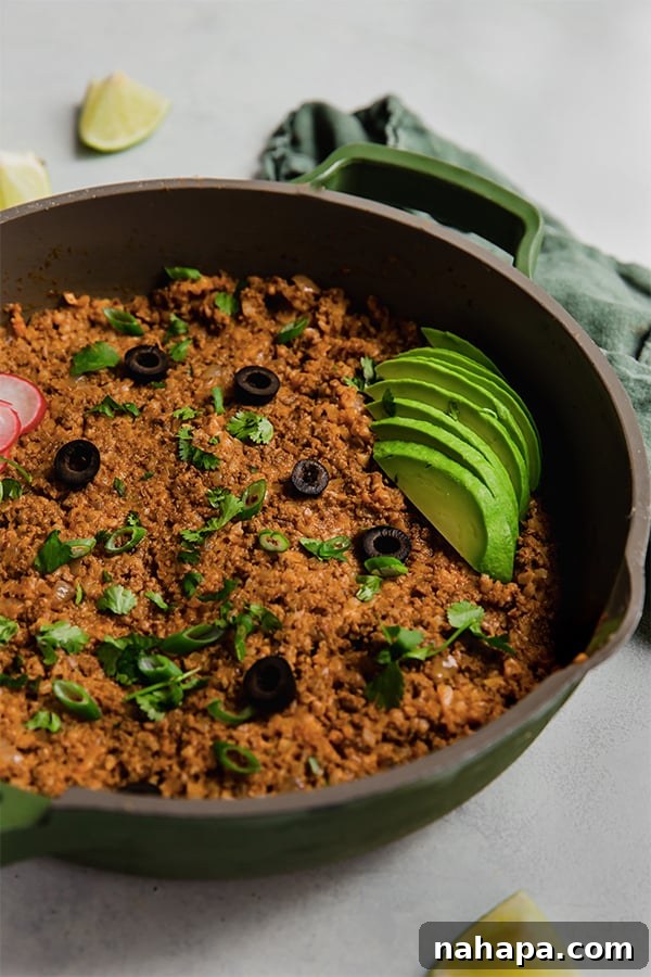 The ground beef and cauliflower rice enchilada mixture simmering robustly in a large cast-iron skillet, ready for serving.