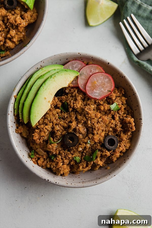 A vibrant bowl of ground beef and cauliflower rice enchilada, generously topped with fresh avocado slices and cilantro, ready to be enjoyed as a wholesome meal.