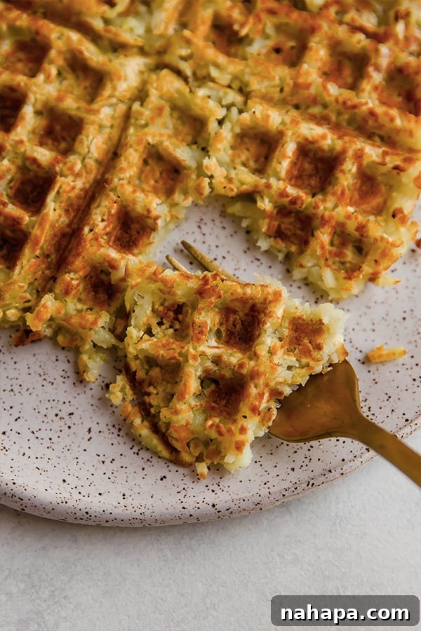 A fork taking a bite out of a sweet potato hashbrown waffle topped with fresh chives, showing the crispy texture.