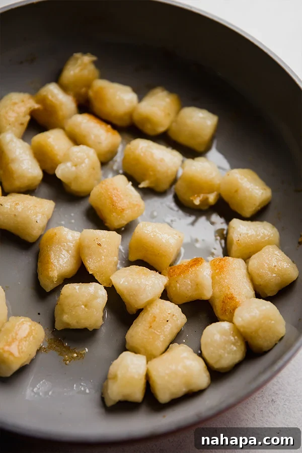 Cauliflower gnocchi cooking in a skillet, turning golden brown.