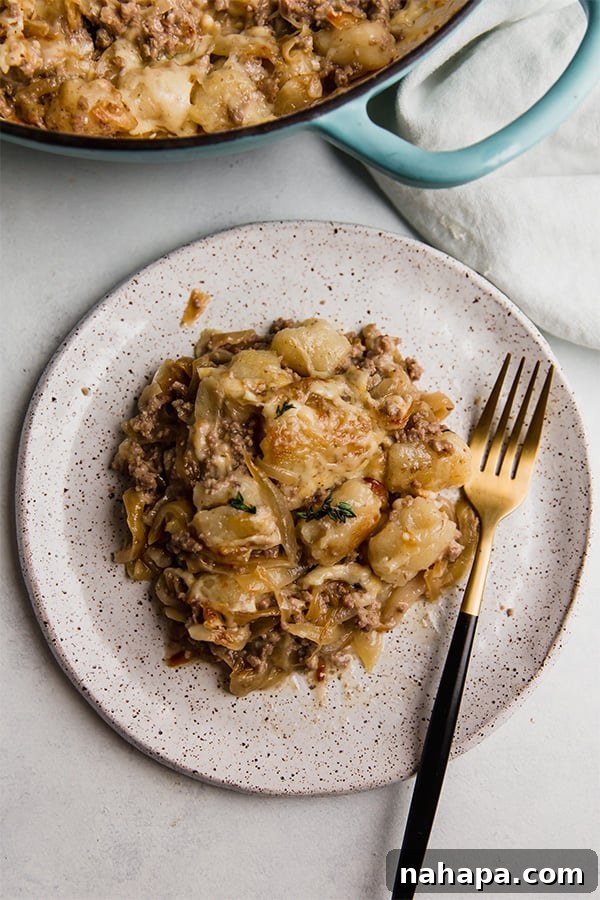 A delicious serving of French Onion Gnocchi Skillet on a white plate, topped with fresh thyme.