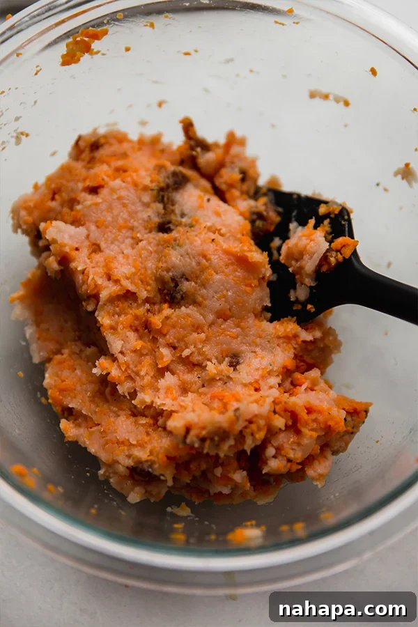 A glass bowl containing the mixed batter for turkey breakfast sausages, showcasing the rich colors of turkey, sweet potato, and dates, ready to be formed.