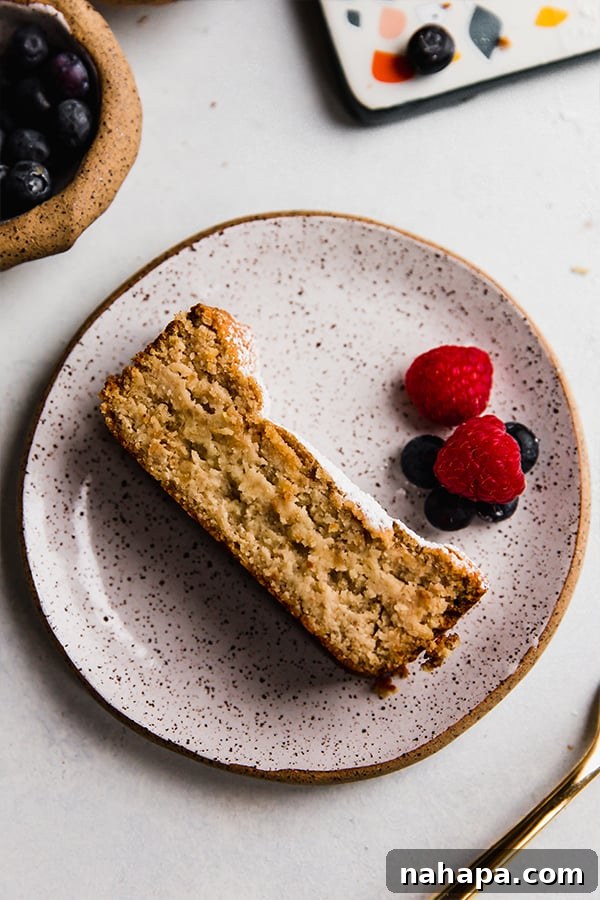 Wholesome Gluten Free Paleo Egg Free Applesauce Pound Cake 2 A slice of moist paleo pound cake on a plate, garnished with fresh berries.
