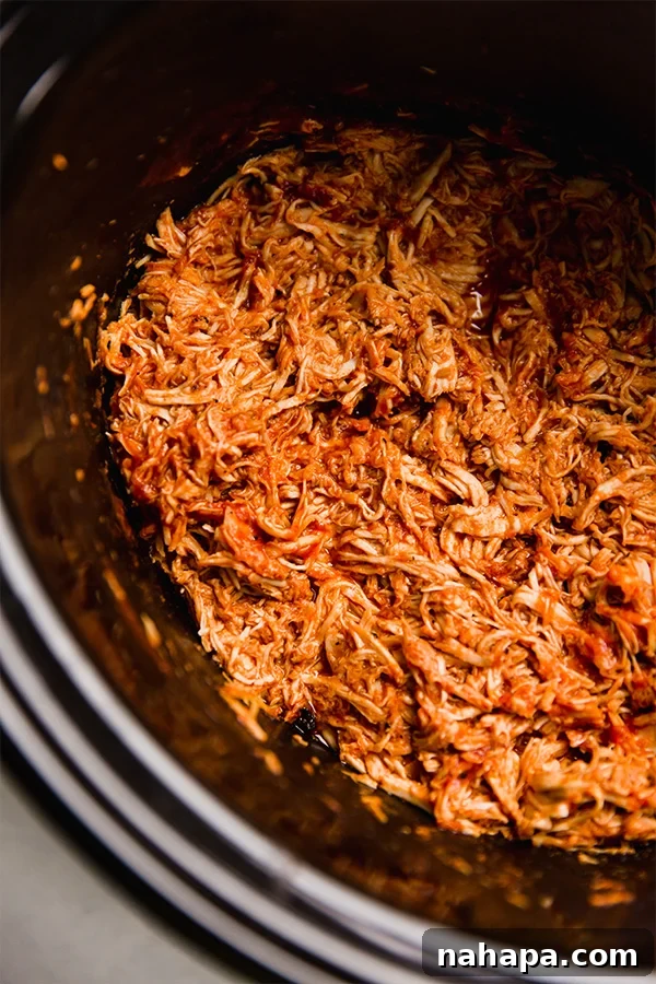 Shredded BBQ chicken cooking in a slow cooker, illustrating the ease of preparation for a delicious meal.