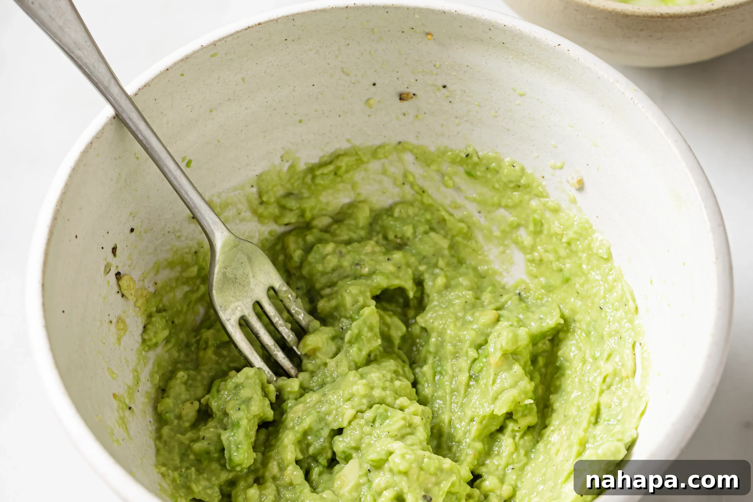 Ripe avocado mashed in a bowl, seasoned with spices and lemon juice, ready for the next step.