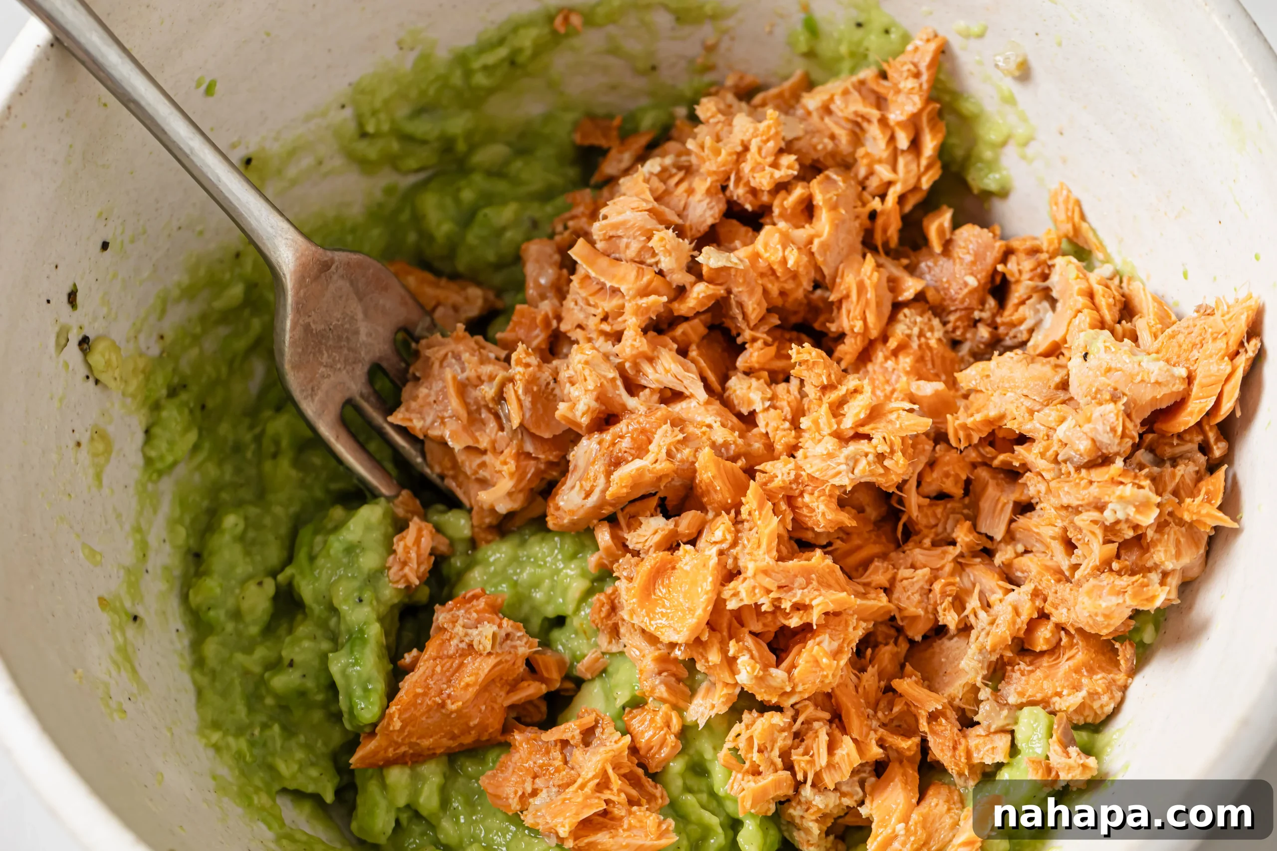 Drained canned salmon added to the mashed avocado in a bowl, awaiting combination.