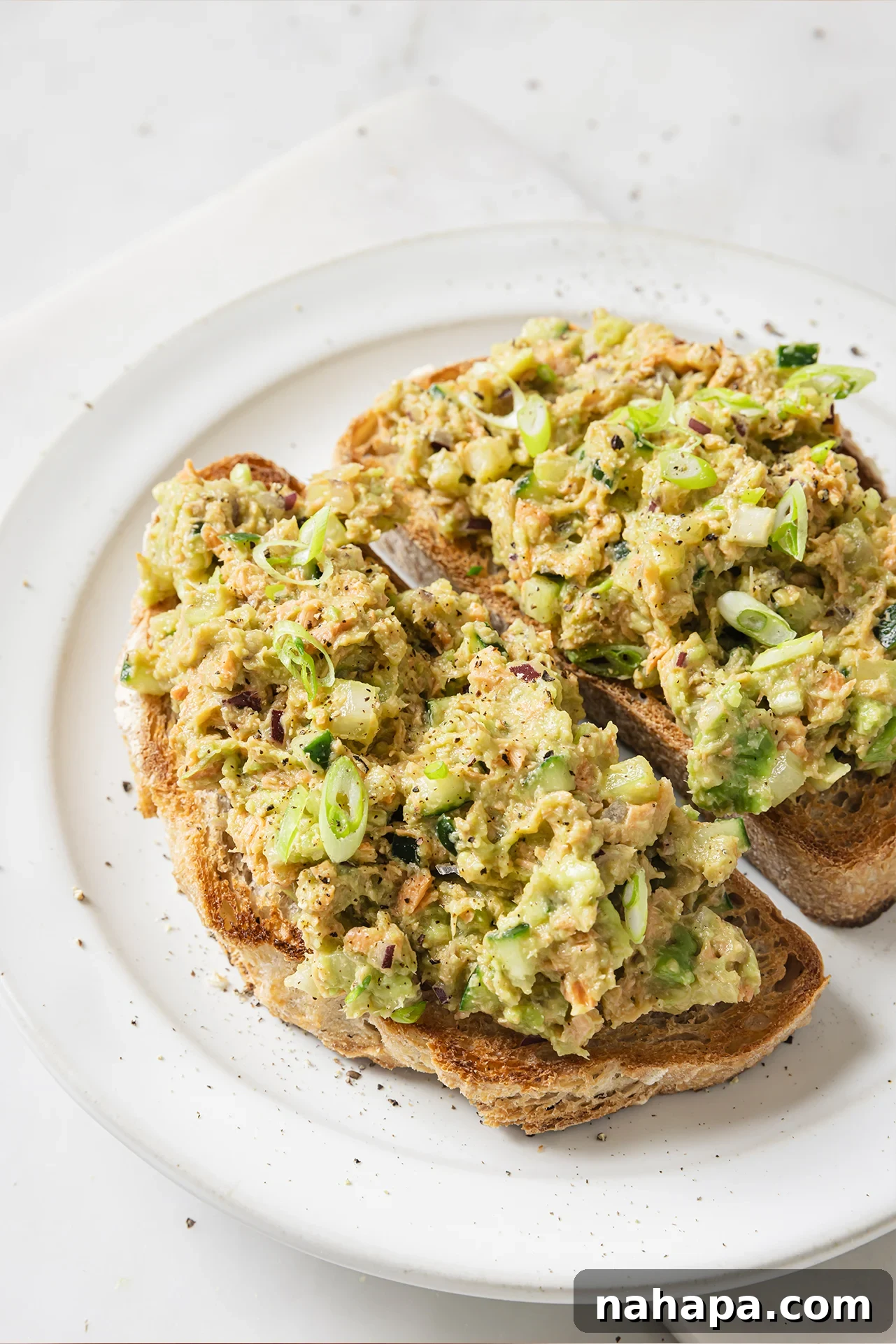 Avocado salmon salad generously spread on two whole slices of crispy toast, ready to be enjoyed.