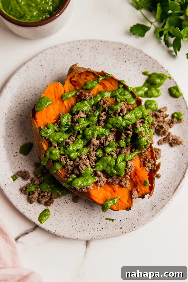 A ground beef stuffed sweet potato with avocado chimichurri on a plate.