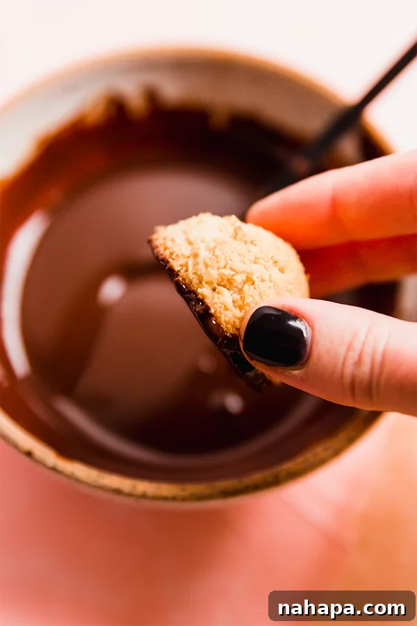 Coconut macaroons being dipped in melted dairy-free chocolate.