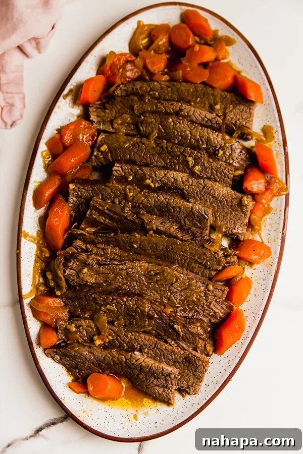 A beautifully sliced oven-roasted brisket on a serving dish, surrounded by tender carrots and onions, ready to be enjoyed.