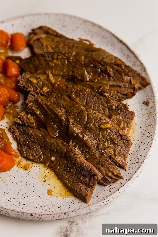 A generous serving of tender brisket slices, accompanied by braised carrots and onions, ready on a dinner plate.