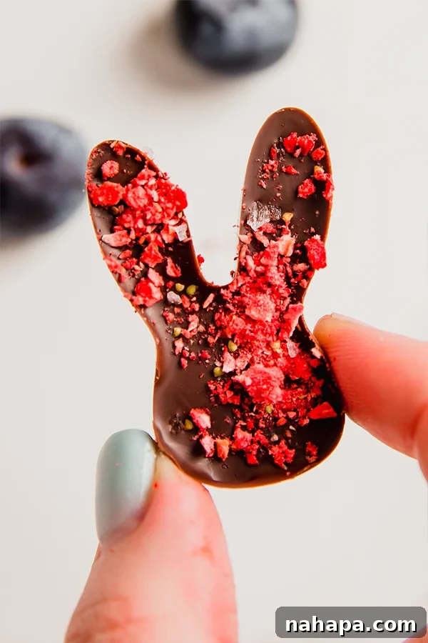 Close-up of one dairy-free chocolate Easter bunny, held between fingers, showcasing the strawberry topping.