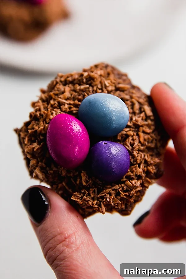 Sweet Coconut Chocolate Easter Nests 6 A single Chocolate Coconut Easter Egg Nest, showcasing its rounded shape and colorful candy eggs, held delicately between fingers.