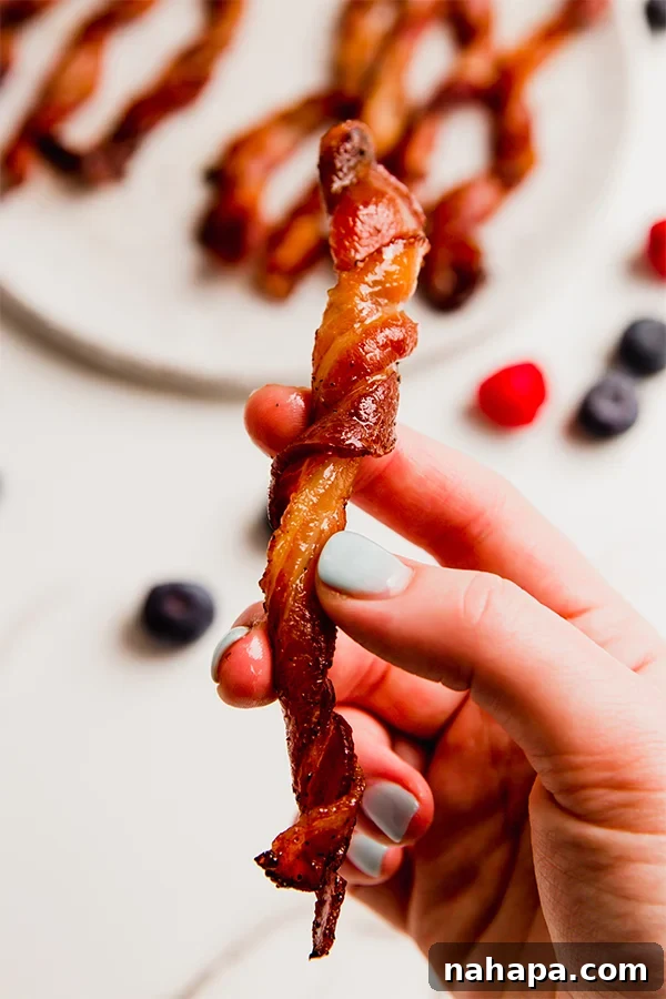 Golden Bacon Spirals 5 A hand holding one oven bacon twist, showing its unique spiral shape and crispy texture.
