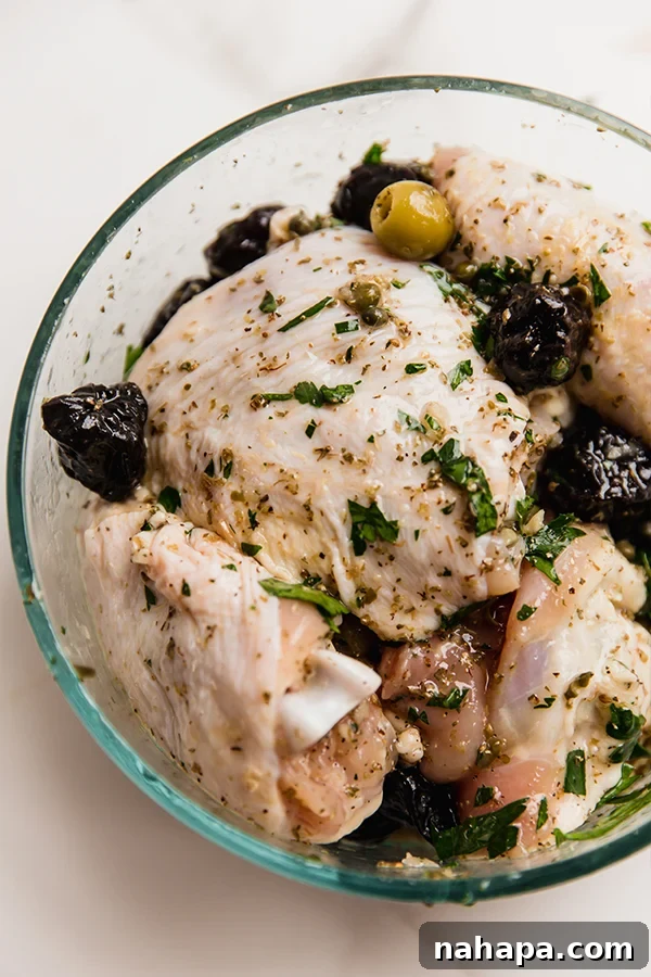 Raw chicken thighs coated in the vibrant marinade with olives, capers, and prunes, ready for cooking.