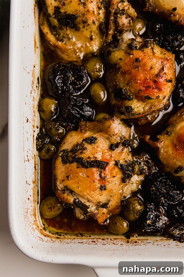 Chicken Marbella baking in a casserole dish, surrounded by the rich sauce, olives, and prunes.