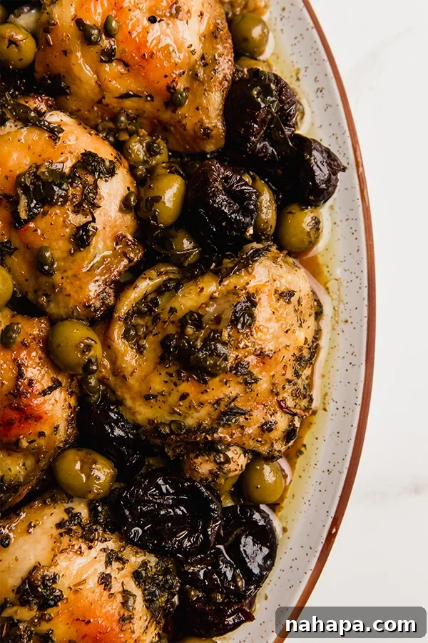 A close-up of a perfectly baked Chicken Marbella on a serving platter, showing the crispy skin, rich sauce, and tender ingredients.