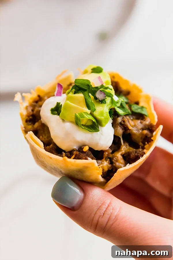 One mini taco cup being held by fingers, showcasing its crispy shell and savory filling.