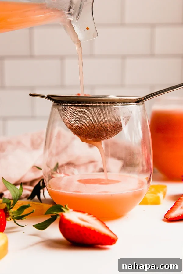 Strawberry Sparkler 3 Straining the strawberry mimosa mocktail through a fine-mesh sieve.
