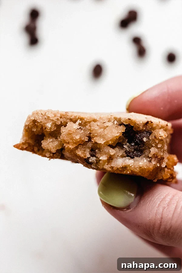 A close-up shot of a baked chocolate chip cookie held between two fingers, showing its soft texture and melted chocolate.