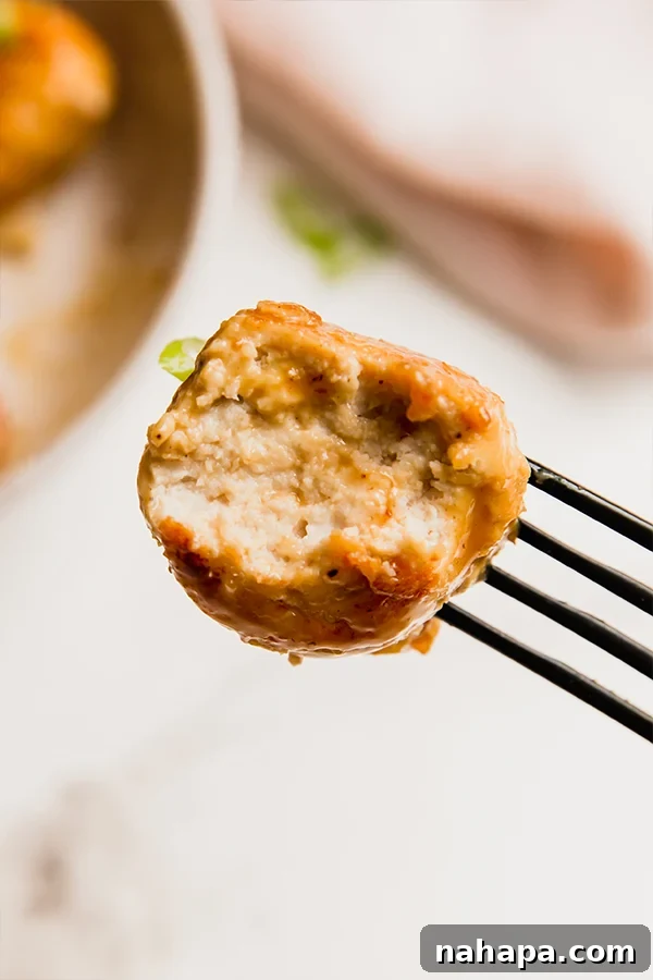 A single orange chicken meatball on a fork, showing its glazed exterior and tender texture.