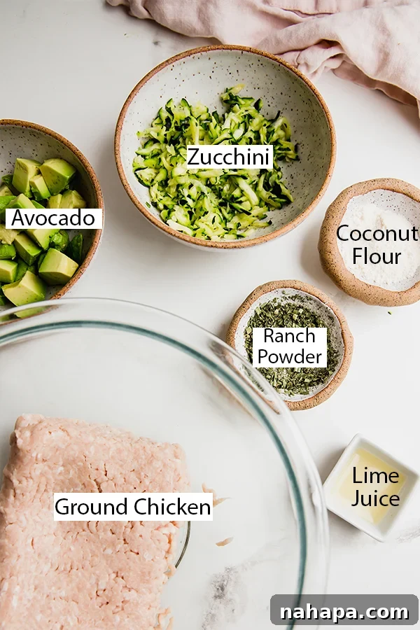 A vibrant display of fresh ingredients laid out, including lean ground chicken, finely shredded zucchini, fresh avocado, and an array of dried herbs and spices, meticulously prepped for making avocado ranch chicken burgers.
