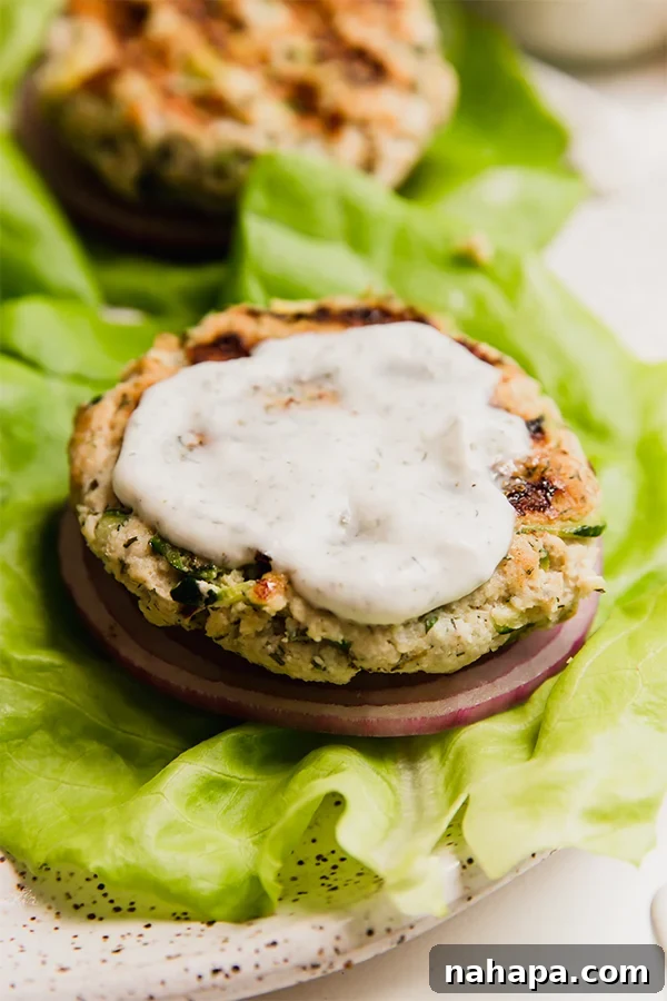 A close-up shot of an avocado ranch chicken burger, perfectly cooked, resting on a crisp lettuce leaf with a swirl of creamy ranch dressing on top, ready to be enjoyed.