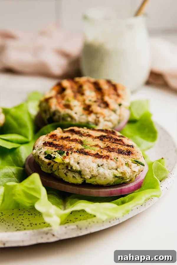 Two avocado ranch chicken burgers presented beautifully on a plate with fresh lettuce leaves, showcasing their appealing texture and vibrant colors.