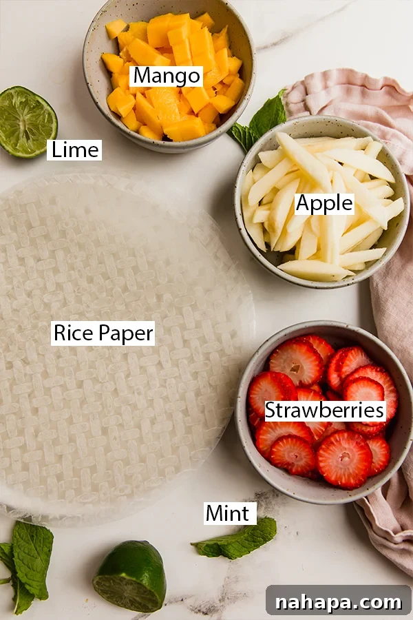 Refreshing Fruit Rice Paper Wraps with Tangy Yogurt Drizzle 3 A collection of fresh ingredients laid out, including rice paper wrappers, mint leaves, sliced strawberries, diced mango, and julienned apple, ready for fruit spring roll preparation.