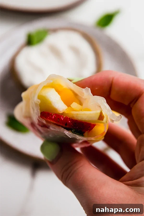 Refreshing Fruit Rice Paper Wraps with Tangy Yogurt Drizzle 5 A freshly made fruit rice paper roll with a small bite taken out, revealing the colorful fruit and mint inside, alongside a bowl of creamy yogurt lime dip.