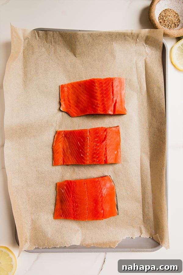 Zesty Peppered Salmon 3 A baking sheet with several raw salmon fillets seasoned with lemon pepper, ready for the oven.