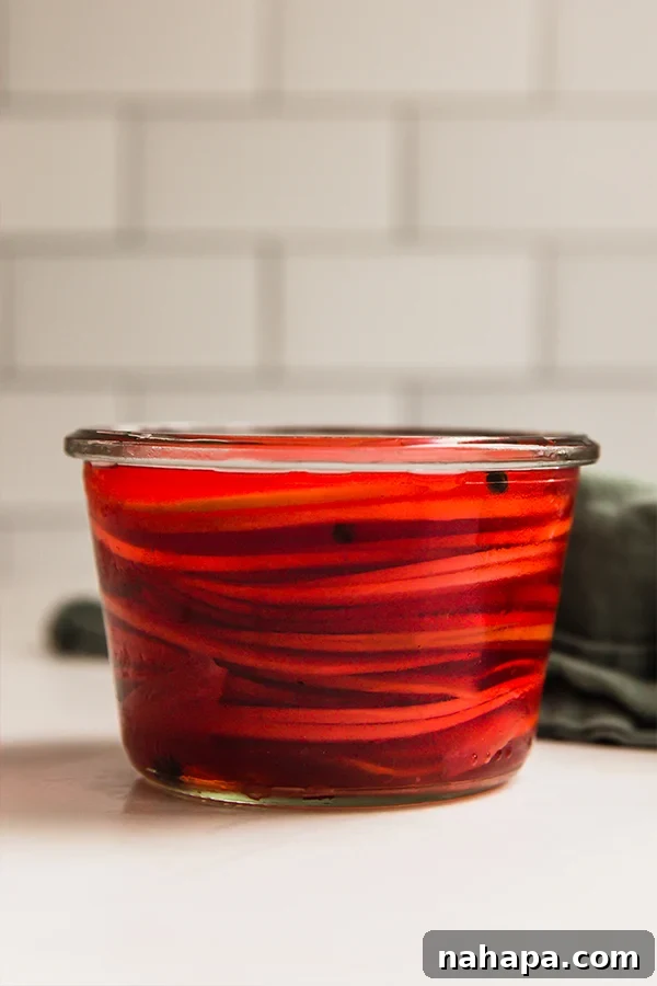 A glass jar filled with vibrant pink pickled watermelon radish slices, showcasing their beauty.