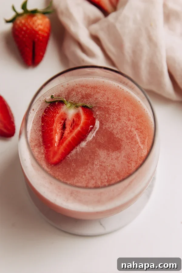 A glass of frosé with a sliced strawberry and a mint leaf as garnish.
