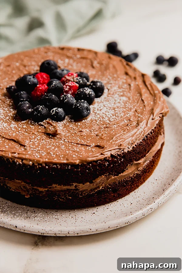 A close-up shot of the full paleo vegan chocolate cake, generously frosted and adorned with vibrant fresh berries, making it an irresistible dessert.