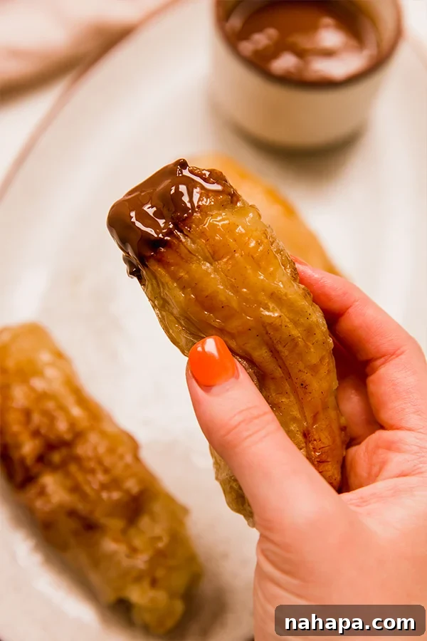 A hand holding a perfectly cooked, golden-brown Filipino Banana Lumpia, showcasing its appealing crispy texture.
