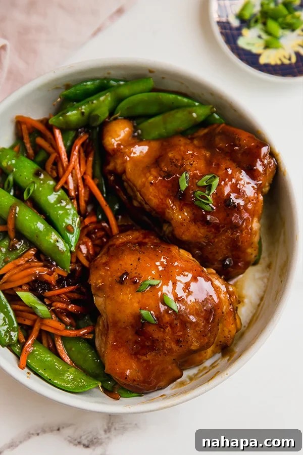 A bowl with vegetables and teriyaki chicken thighs, garnished with fresh herbs.