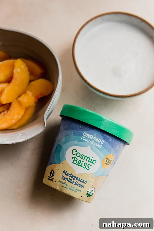 All the fresh and healthy ingredients neatly laid out for making a dairy-free creamy peach milkshake: frozen peach slices, a can of coconut milk, dairy-free vanilla ice cream, and a small bowl of cinnamon.