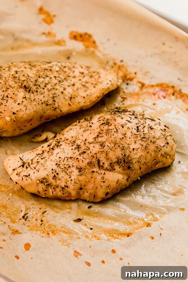 Chicken breasts seasoned with herbs on a baking sheet lined with parchment paper.