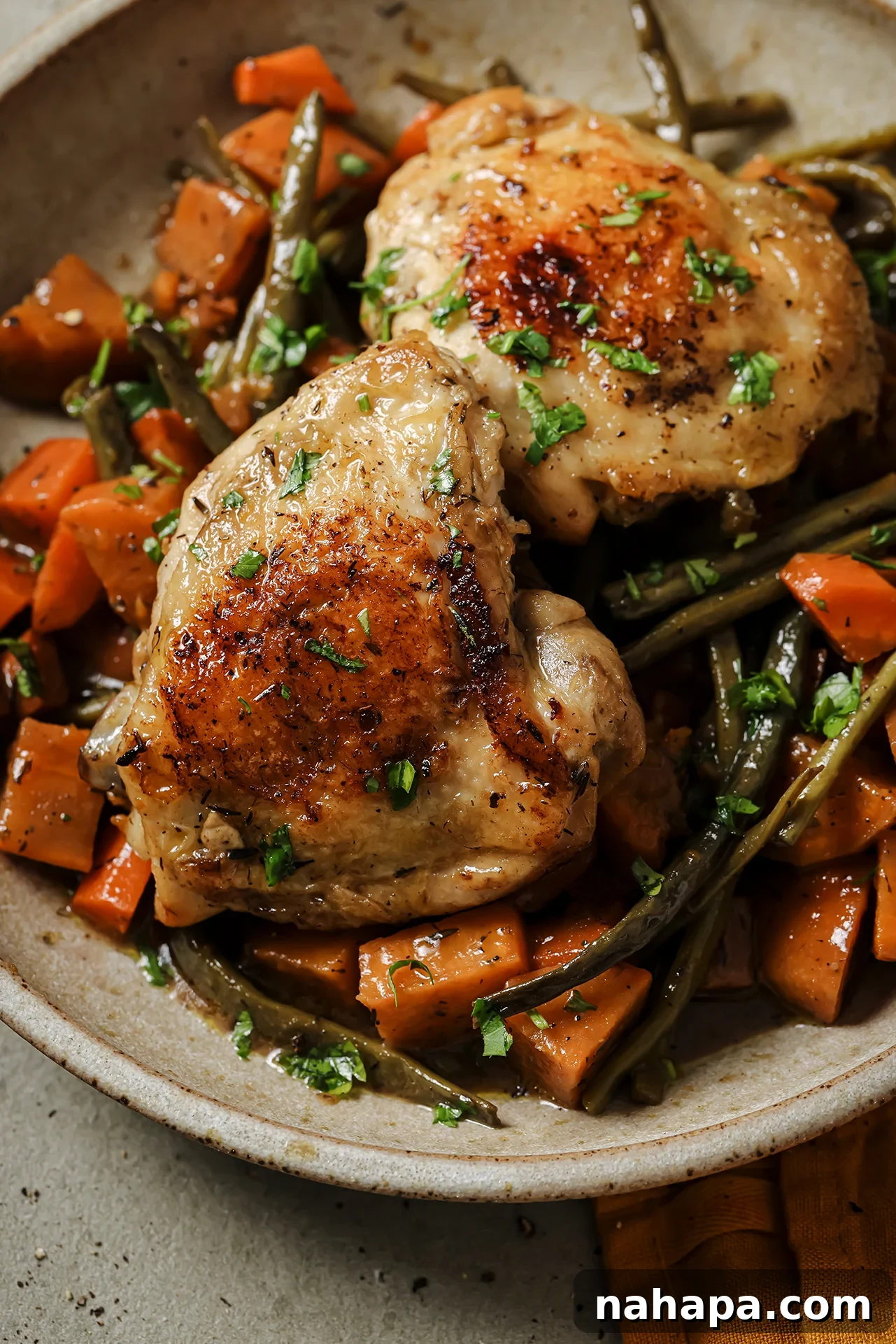A rustic bowl filled with slow cooker balsamic chicken, sweet potatoes, carrots, and green beans, garnished with fresh herbs.