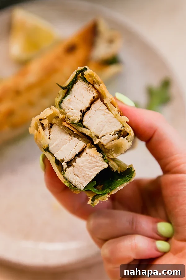 A gluten-free chicken pesto wrap, cut in half to reveal the vibrant filling, displayed on a wooden surface.