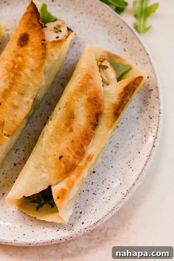 Two freshly made gluten-free chicken pesto wraps, cut in half, elegantly presented on a white plate with a fork.