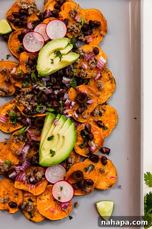 A beautifully assembled baking sheet of sweet potato nachos, laden with ground beef and colorful toppings, ready to be served.