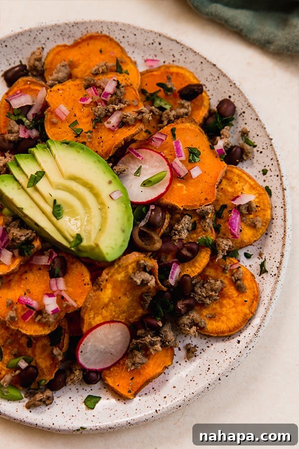A close-up of a plate of healthy sweet potato nachos, garnished with fresh herbs and a lime wedge.