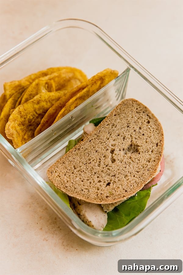 One adult lunchable container, showcasing a chicken sandwich, plantain chips, and apple slices.