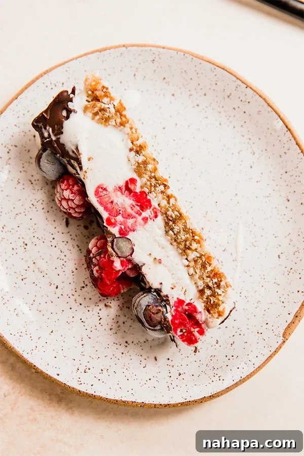 A freshly sliced piece of gluten and dairy-free no-bake berry vanilla ice cream cake on a plate, garnished with fresh berries.