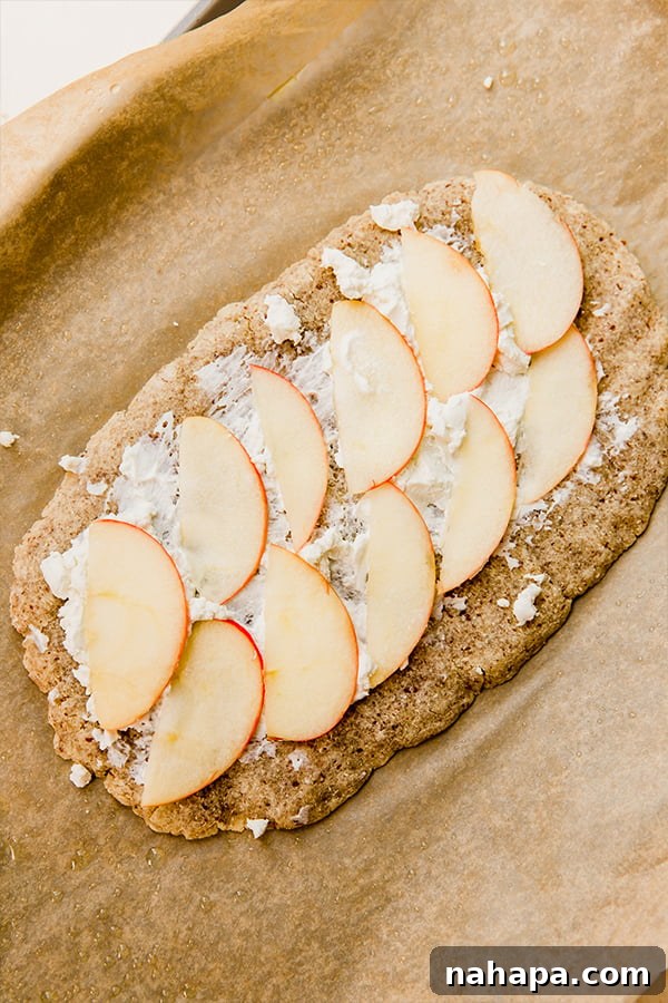 A partially baked apple balsamic flatbread, topped with melted cheese and thinly sliced apples, ready for its final additions.