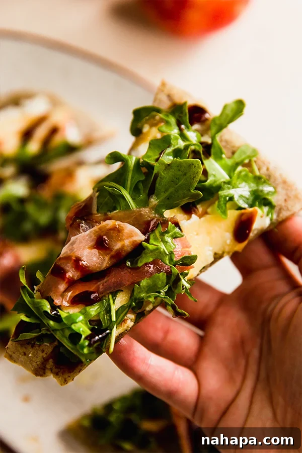 A close-up shot of a hand holding a slice of gluten-free apple balsamic flatbread, showcasing its delicious layers.