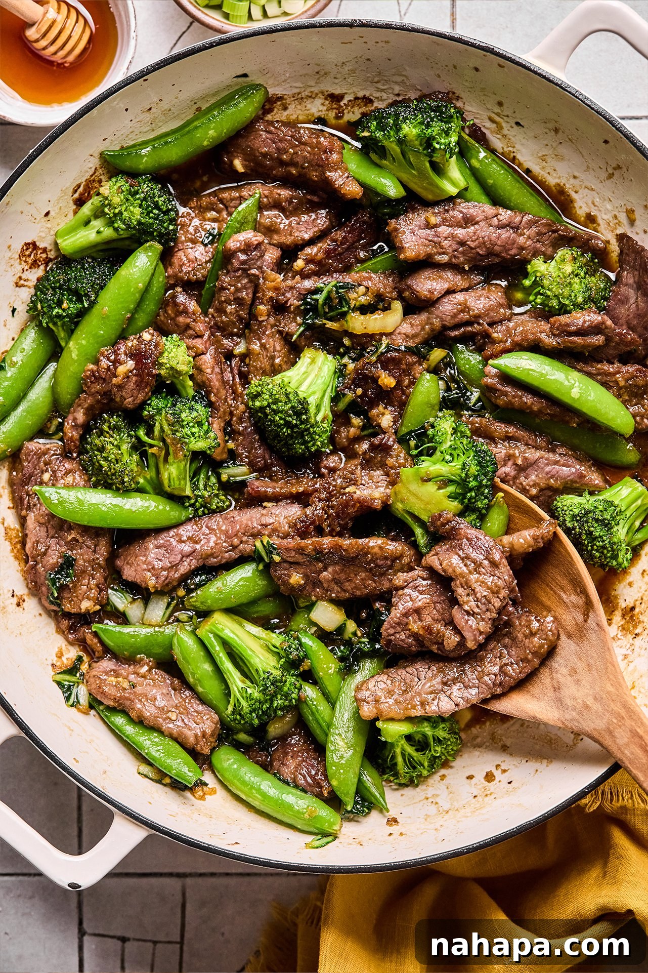 Honey garlic beef stir fry in a pan with a wooden spoon, showcasing rich flavors and vibrant vegetables.